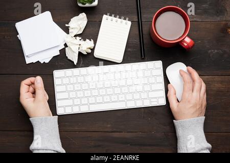 white wireless keyboard and mouse on a wooden brown table, next to a white cup with coffee Stock Photo