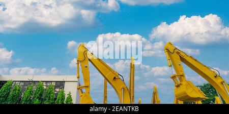 Yellow backhoe with hydraulic piston arm against blue sky. Huge bulldozer parked at parking lot near sale office. Bulldozer dealership. Hydraulic machinery. Heavy machine industry. Stock of backhoe. Stock Photo