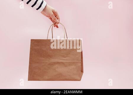 Hand holding craft paper bag on pink background. Stock Photo