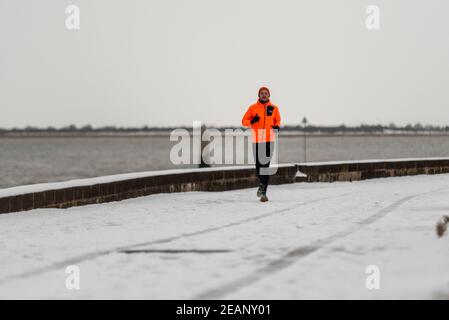 Lone male runner running on snow by seafront in Southend on Sea, Essex, UK, during Storm Darcy weather event. Icy seaside promenade. Slippery surface Stock Photo