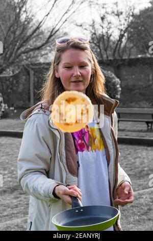 Woman tossing pancake at Pancakes on the Pavilion pancake race on Shrove Tuesday at Christchurch, Bournemouth, Dorset UK in March Stock Photo