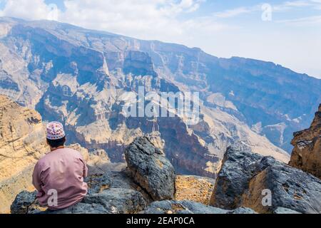 A man is sitting on the edge of 'the grand canyon of middle east' at the Jebel Shams mountain in Oman