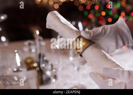 A white-gloved waiter holds a tissue napkin and a vintage ring in her hands. Photos without a face.Christmas tree out of focus. Copy space. Macro photo in the interior Stock Photo