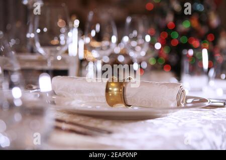 An antique yellow metal ring is attached to a cloth napkin. Table setting for the New year. The Christmas tree is out of focus. Copy space. Stock Photo
