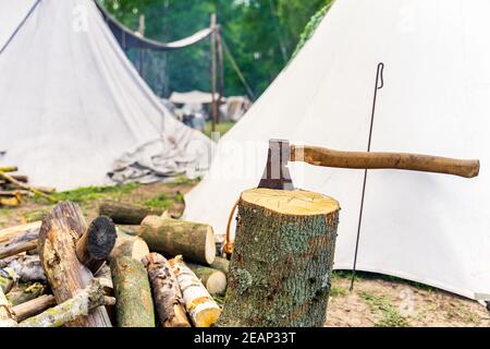 An axe stuck in the stump of a tree with chopped logs Stock Photo