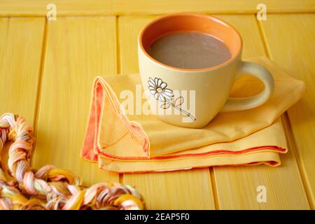 Cappuccino with coffee art in orange cup on yellow wooden table. Stock Photo