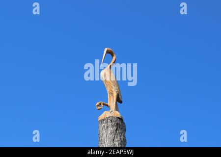 Figure of crane on the stump of a tree against the blue sky. Figures of animals made of wood. Woodcarving Stock Photo