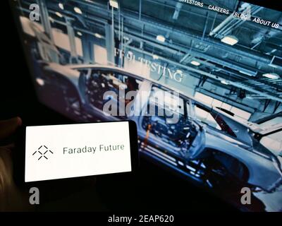 Person holding smartphone with logo of American electric vehicle company Faraday Future Inc. in front of website. Focus on phone display. Stock Photo