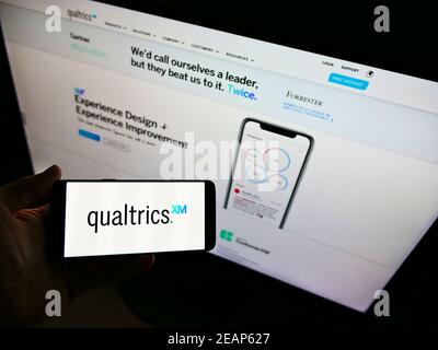 Person holding smartphone with logo of American software company Qualtrics International Inc. in front of website. Focus on phone display. Stock Photo