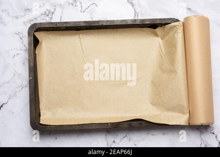 rectangular metal baking sheet and roll of brown parchment paper on white background Stock Photo