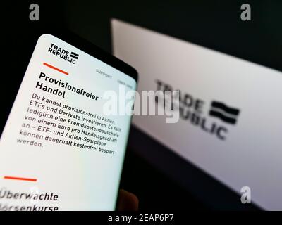Person holding cellphone with web page of German online broker Trade Republic on screen with company logo. Focus on top-left of phone display. Stock Photo