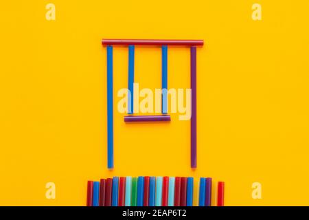Children swing made of cocktail tubes, orange background Stock Photo