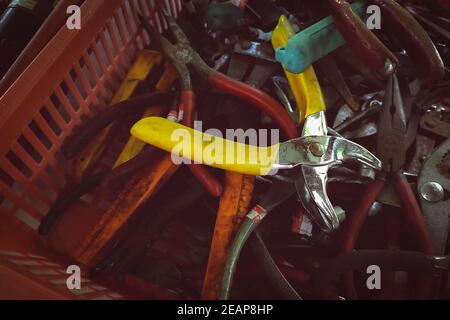 Old pliers in plastic basket. Second-hand tool for sale at tools market. Old pliers in tool tray. Toolkit of handyman. Mechanic hand tools. Used tools in second-hand market, Thailand. Many of pliers. Stock Photo