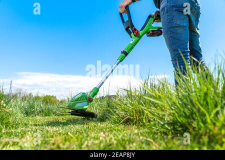 man mows the grass in the meadow with a hand-held cordless lawnmower Stock Photo