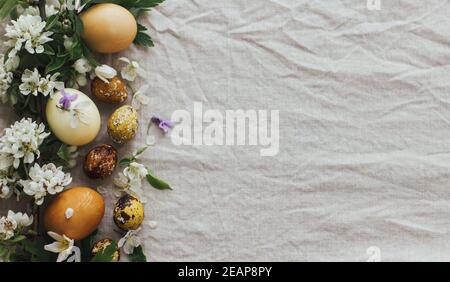 Easter eggs with spring flowers on rustic linen background, flat lay with space for text. Stylish modern easter and quail eggs with natural dye and sp Stock Photo