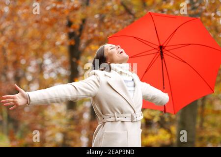 Excited woman with red umbrella celebrating vacation in a forest under ...