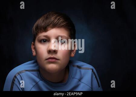 portrait of a serious european teenage boy with light brown hair, dressed in a light blue turquoise sports t-shirt, on an isolated background Stock Photo