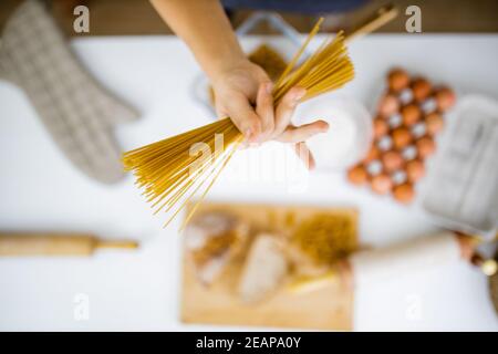 Female hand holding uncooked spaghetti above ingredients on a table Stock Photo