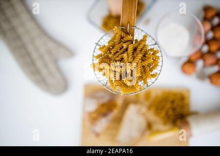 Uncooked fusilli on wooden pasta strainer above ingredients on a table Stock Photo