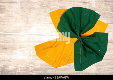 Top view of a folded yellow and green kitchen cloth, textile, tablecloth or napkin on blurred wooden background. Template for your food and product display montage. Stock Photo