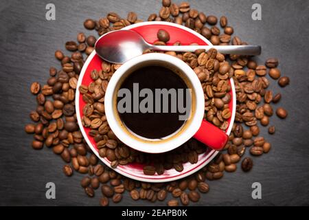 Red cup of coffee with coffee beans on dark textured background. Morning fresh energy concept.