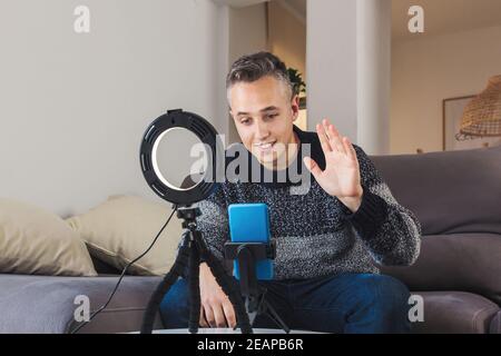 Stock photo of Young man millennial influencer sit on couch is vlogging, recording and creating online content with smartphone and lights. Social medi Stock Photo