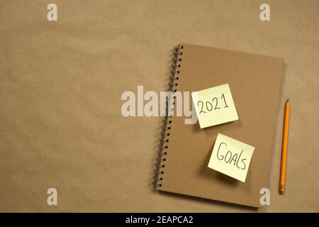 Notebook with yellow sticky notes with 2021 and goals for New Year on brown paper background with classic pencil, business or school, education concept. Copy space Stock Photo