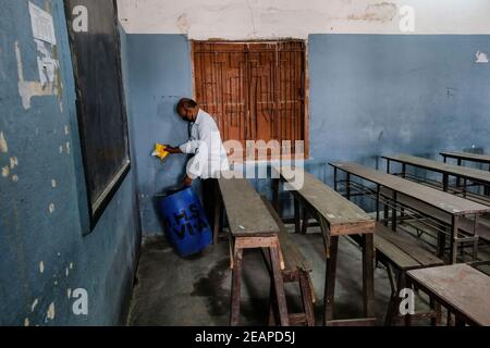 A staff member of Madhyamgram high school wearing a face mask disinfects a classroom as the school prepares to reopen. The west Bengal government has decided to reopen schools across the state with proper covid 19 guidelines from 12th February. The schools will reopen for Classes 9 to 12 after ten months of being shut since March 16, 2020 due to the coronavirus pandemic. The state government has said that students will only be allowed to attend offline classes with parental consent. Stock Photo