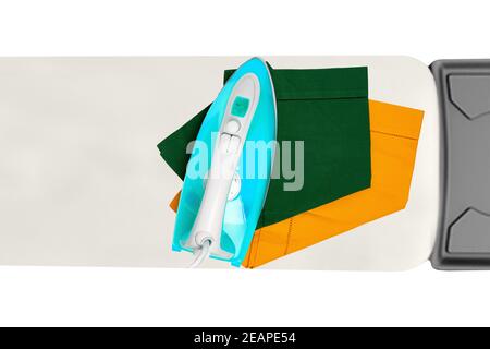 Top view of a modern electric blue iron ironing a green and a yellow cloth napkin on an ironing board indoors isolated. Advertising for the laundry service with space. Stock Photo