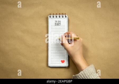 Top view 2021 human hand with notepad New year goals or planning on brown plain paper background, copy space modern design, business or school background Stock Photo