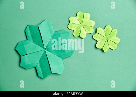 Origami four-leaf shamrocks, made of green paper, on green background. Concepts of luck and St. Patrick's Day. Image with copy space. Stock Photo