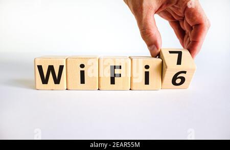 WiFi 6 or 7 symbol. Businessman turns a wooden cube and changes the words WiFi 6 to WiFi 7. Beautiful white background, copy space. Business, technolo Stock Photo