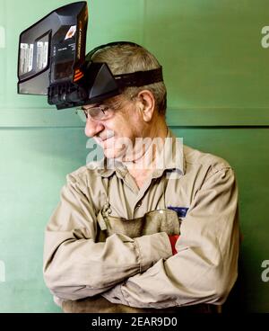 Man in work attire and welding mask smiling looking sideways. Stock Photo
