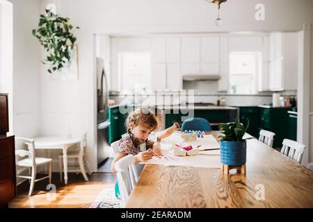 Two young kids doing arts and crafts in modern dining room. Stock Photo