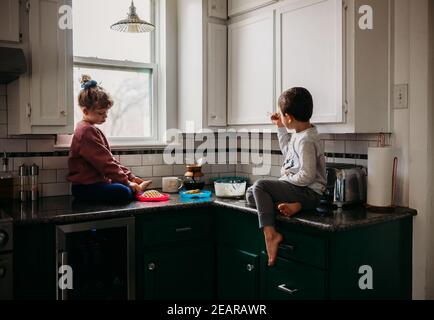Brother and sister sitting in kitchen together eating waffles Stock Photo