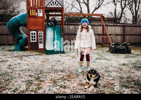Two young kids and puppy playing in backyard on snowy day Stock Photo
