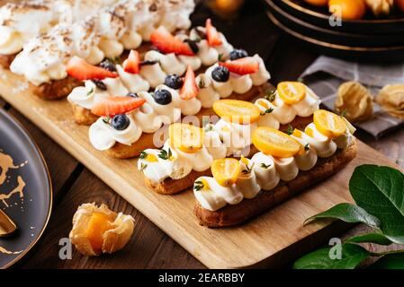 Freshly baked delicious eclairs with berries on a wooden olive board Stock Photo