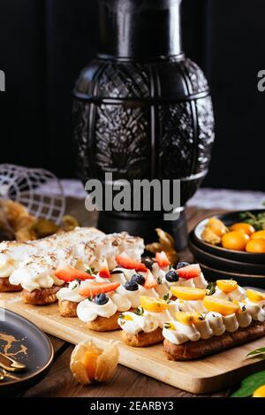 Freshly baked delicious eclairs with berries on a wooden olive board Stock Photo