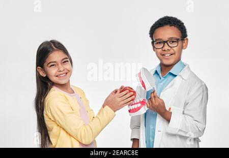 Child dental health. Funny boy and girl bites an apple using human teeth jaw model Stock Photo