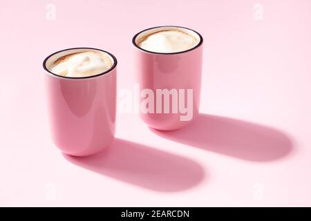 Two cups of cappuccino in pink cups on pink background Stock Photo