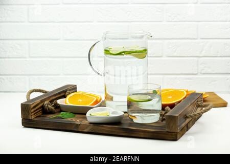 A home made lemonade made of lime stands in a glass and jug on a wooden tray with oranges around Stock Photo