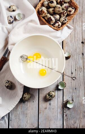 Broken quail eggs in a bowl on a wooden background. Stock Photo