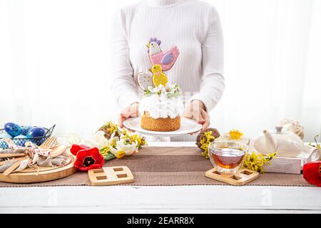Women's hands are holding a festive Easter cake, decorated with flowers and bright details. The concept of preparing for the Easter holiday. Stock Photo