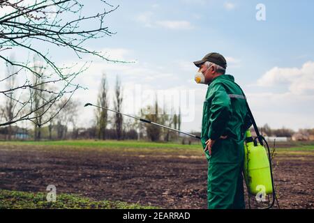 Senior farmer spraying tree with manual pesticide sprayer against insects in spring garden. Agriculture and gardening concept Stock Photo
