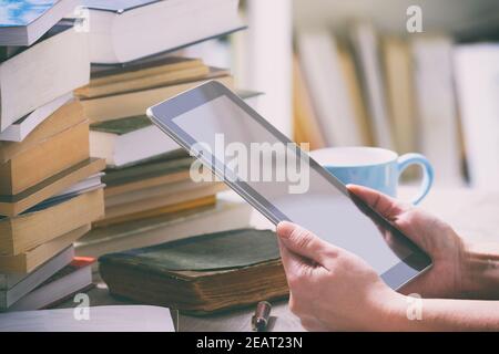 Man holding a modern ebook reader in hands on a table with piles of books Stock Photo