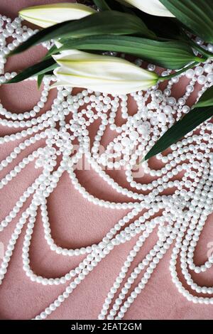 White lilies with green leaves and a necklace of pearls on a pink background. Stock Photo
