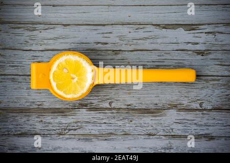 Half a lemon in a yellow squeezer on a light blue wooden backdrop. Stock Photo