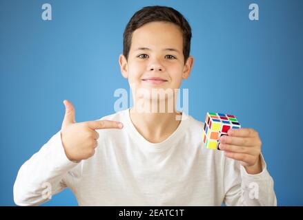Young boy plays with rubik's cube over blue background Stock Photo