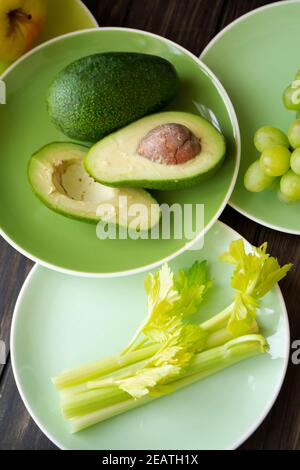 Healthy eating vegan produce. Green vegetables and fruits on green plates. Avocado, green apples, grapes and celery Stock Photo