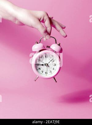 A woman's hand holds a pink alarm clock against a pastel background Stock Photo